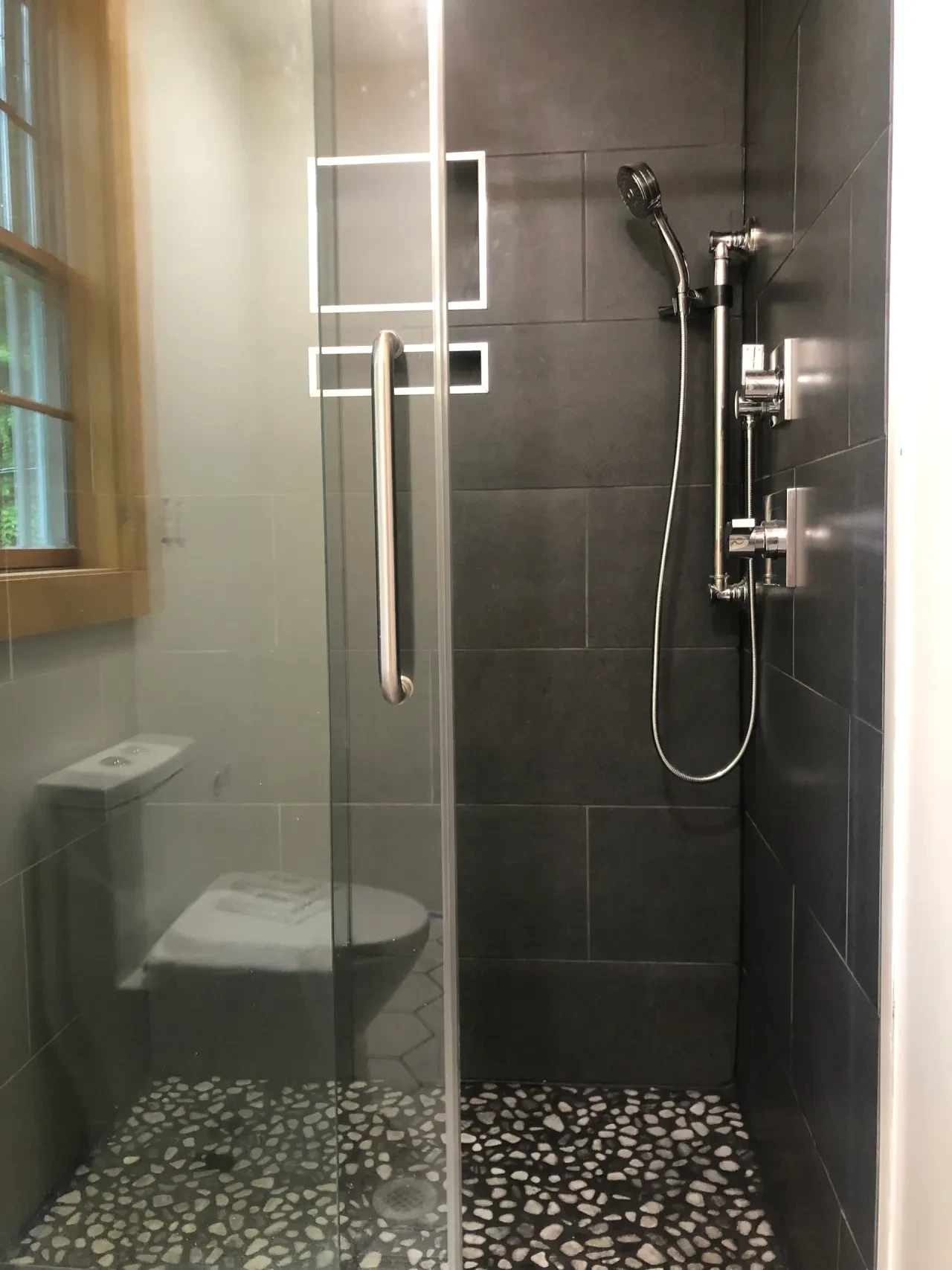 Finished pebble floor shower with dark tile surround and glass door